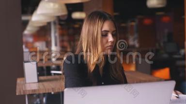 严肃的女商人穿着黑色衬衫在笔记本电脑上工作，在笔记本上记笔记